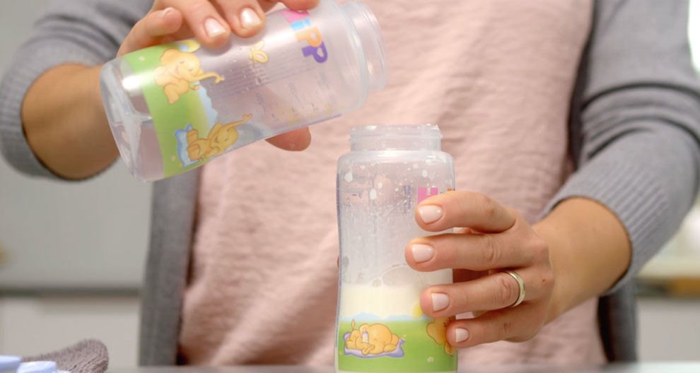 A person is pouring a liquid from a colorful baby bottle into another bottle.