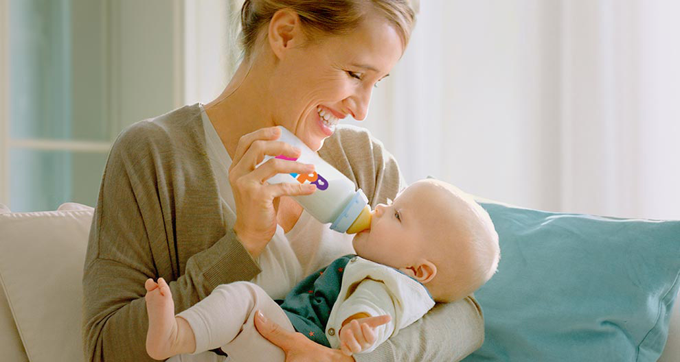 A woman in a gray cardigan is feeding a baby with a bottle.