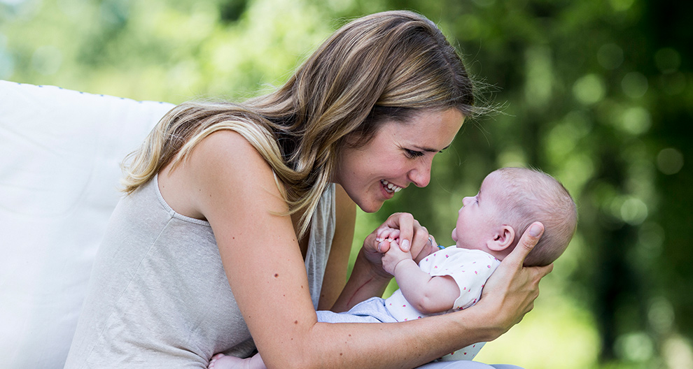 A woman holds a baby outdoors.