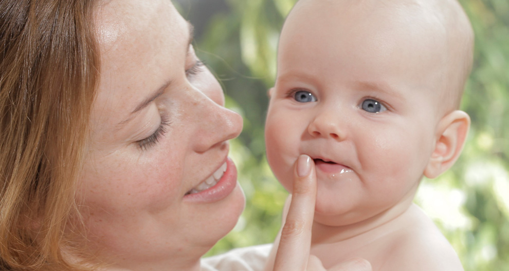 A woman is holding a baby, who is chewing on the woman's finger.