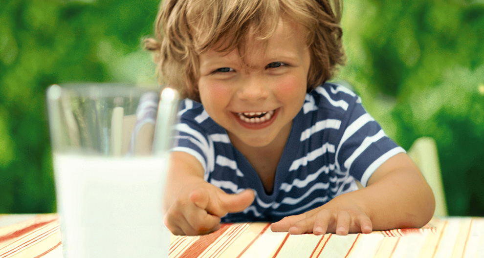 A child in a striped shirt is reaching out towards a glass of milk.
