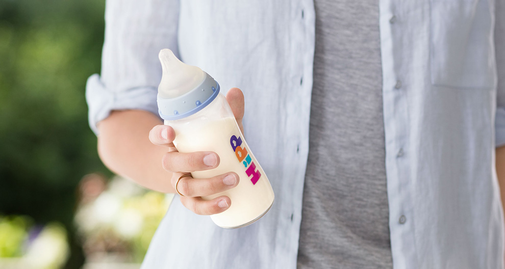 A person in a light blue shirt holds a baby bottle with a colorful label.