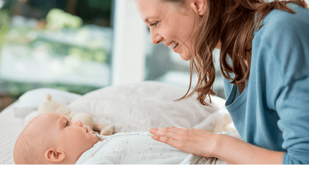 A woman in a blue shirt is looking at a baby lying on a bed.